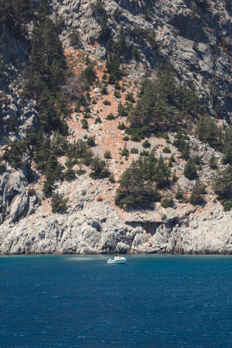 A yacht sailing near the scenic rocky coastline of Rhodes, Greece.