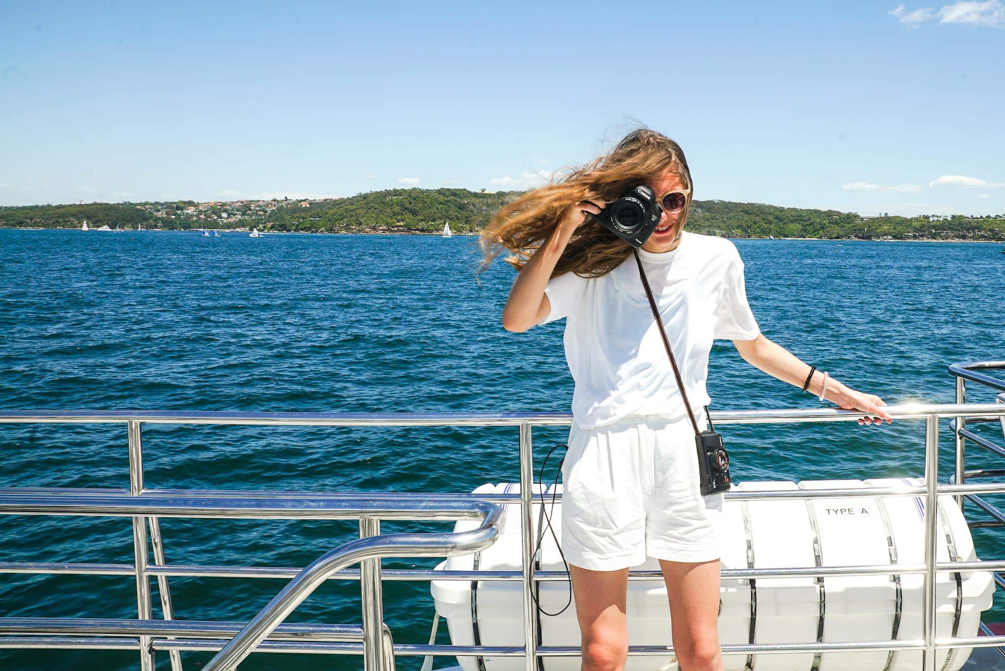 Young woman on a yacht capturing moments with a camera on a sunny day at sea.
